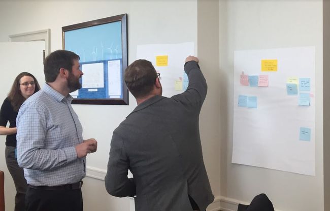 team members standing at a wall of sticky notes that contain job tasks to be performed by internal team members